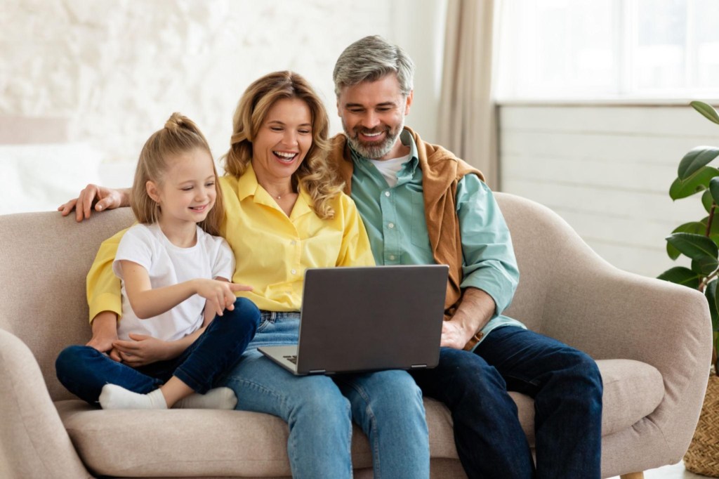 Parents happily watching on the laptop with their little child while seated on the couch